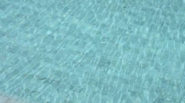 Yavaş çekim, berrak su dalgalanması mavi yüzme havuzunda beyaz fayanslı zemin