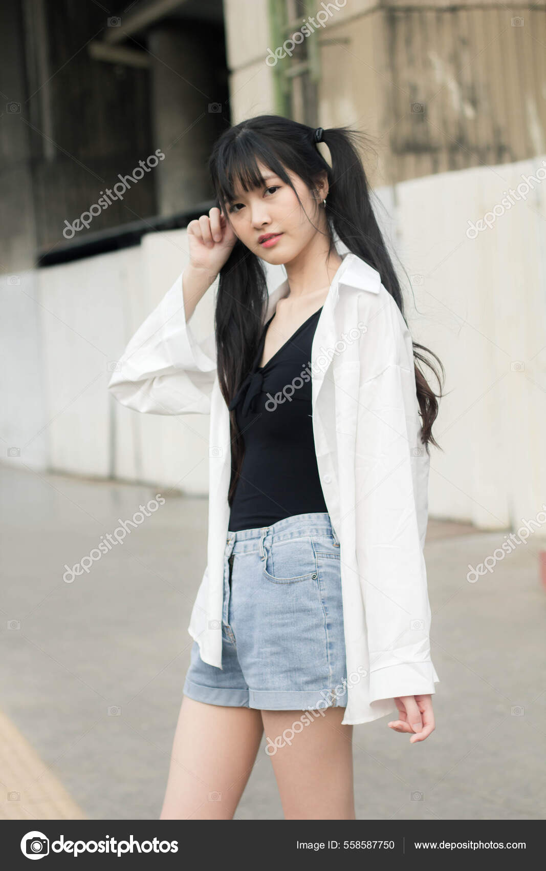 A Street Photo Of A Young Beautiful Female Wearing White T-shirt And Black  Jeans Shorts Standing On The Old Building Background. Empty Space For Text  Or Design. Outdoor. Stock Photo, Picture and