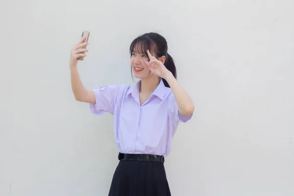 アジアタイ高校生制服美少女使用彼女のスマートフォンSelfie — ストック写真