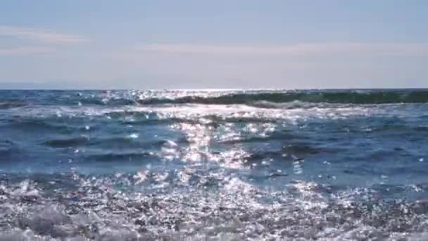 Små vågor rullar in på stranden. Solen reflekteras i havsvattnet. — Stockvideo