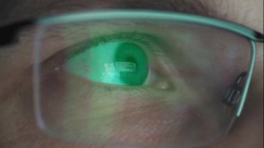 Zaman ayarlı makro çekim, gözlüklü bir adamın yorgun gözleri bilgisayar ekranına bakıyor. Parlak ekran gözlüklerin lenslerine yansıyor. Geceleri bilgisayarda çalışan bir adam..