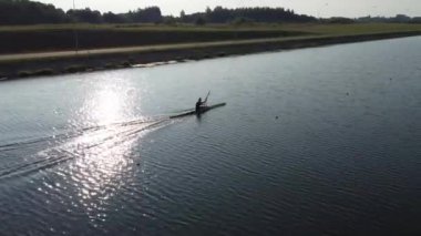 Profesyonel bir kürekçinin batan güneşin ışınlarında kanoyla kürek çekişini gösteren hava manzarası..