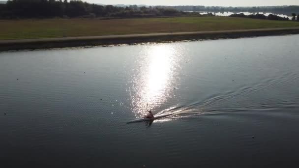 Aerial view of a professional sportsman rower sailing on a rowing canal in a kayak in the rays of the setting sun. — Stock Video