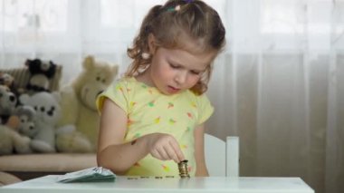 Çocuk kız birikimlerini sayar ve bozuk paraları yığar. Çocuk ekonomisi kavramı, tasarruf.