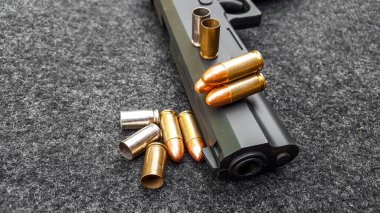 Siyah yapay tabanca ve koyu gri kumaş üzerinde mermiler. Sosyal, kişisel ve atış sporu ekipmanlarının güvenliği kavramı