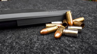 Siyah yapay tabanca ve koyu gri kumaş üzerinde mermiler. Sosyal, kişisel ve atış sporu ekipmanlarının güvenliği kavramı
