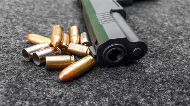Siyah yapay tabanca ve koyu gri kumaş üzerinde mermiler. Sosyal, kişisel ve atış sporu ekipmanlarının güvenliği kavramı