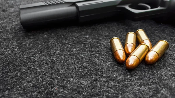 Siyah yapay tabanca ve koyu gri kumaş üzerinde mermiler. Sosyal, kişisel ve atış sporu ekipmanlarının güvenliği kavramı