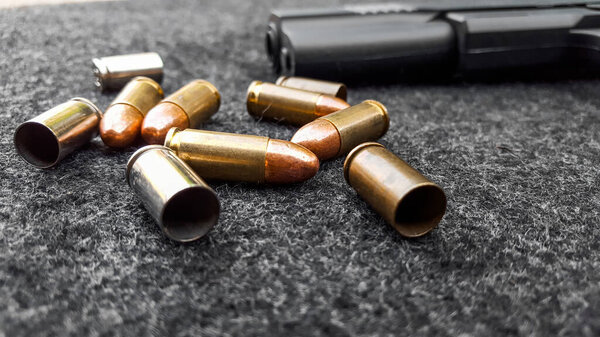 Black artificial handgun and bullets on dark gray fabric. Concept for security of social, personal and shooting sport equipment