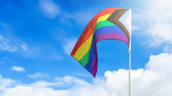 LGBT gökkuşağı bayrağı dalgalanıyor ve dünya çapında LGBTQ + topluluğunu geliştirmek için arka planda mavi gökyüzü var.
