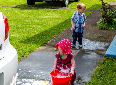 Çocuklar arabayı yıkamaya, suda oynamaya ve köpüklenmeye yardım ediyor. Taranaki, Yeni Zelanda