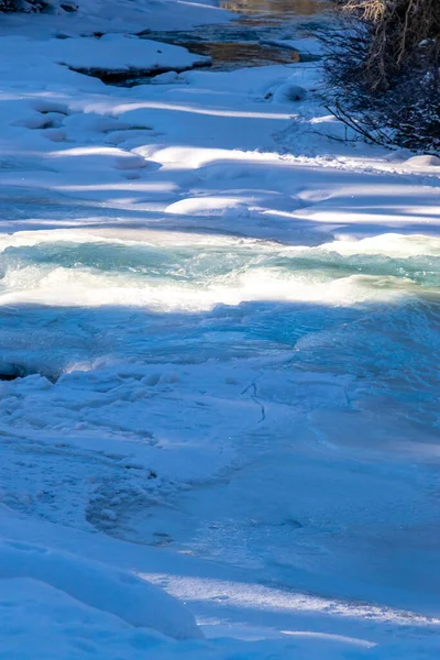 Baker Creek 'in yeşil suları karla kaplı kıyıları geçiyor. Banff Ulusal Parkı, Alberta, Kanada