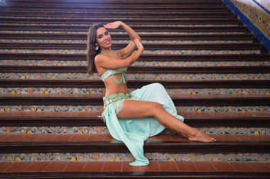 Genç ve güzel dansçı bir merdivende oturmuş dans mankeni pozları veriyor. Dansçı kırmızı bir elbise giyiyor. Göbek dansı konsepti.