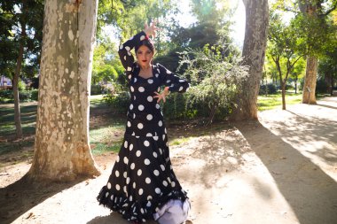 İspanyol, güzel, esmer flamenko dansçısı tipik siyah benekli flamenko elbisesi var. O, Sevilla 'daki parkta dans ediyor. Flamenko kavramı insanlığın kültürel mirası.