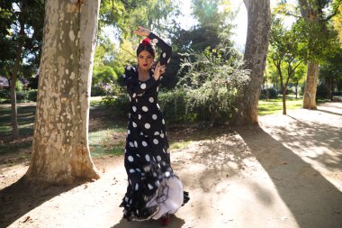 İspanyol, güzel, esmer flamenko dansçısı tipik siyah benekli flamenko elbisesi var. O, Sevilla 'daki parkta dans ediyor. Flamenko kavramı insanlığın kültürel mirası.