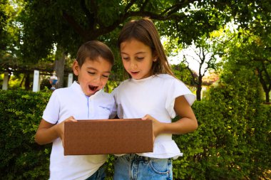 Şaşırmış oğlan ve kız, karton kutuyu açıyor ve içine bakıyor ve bir ışık çıkıyor. Paket, teslimat, sürpriz, hediye yaşam tarzı konsepti. Duygusal ifadelerin kavramları