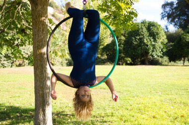 Sarışın kadın ve genç jimnastikçi akrobat sporcu parkta hava halkası üzerinde egzersiz yapıyorlar. Mavi kostümlü kıvrak kadın sirk sanatçılarının kalçalarıyla dans edişini canlandırıyor..