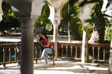Güzel, siyah saçlı, kıvırcık saçlı, Latin hatları olan yetişkin bir kadın bir bankta oturuyor ve piercingli ama ciddi bir bakışla. Ciddi ve kızgın bir kadın kavramı.