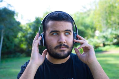 Yakışıklı, Latin, esmer, sakallı, yeşil gözlü bir adam bir çift kablosuz kulaklıkla müzik dinliyor. Boş zaman ve müzik kavramı.