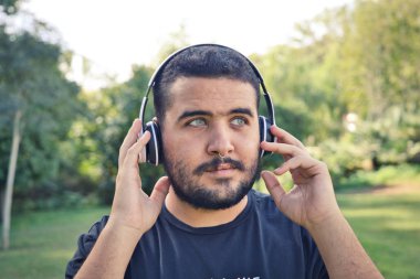 Yakışıklı, Latin, esmer, sakallı, yeşil gözlü bir adam bir çift kablosuz kulaklıkla müzik dinliyor. Boş zaman ve müzik kavramı.