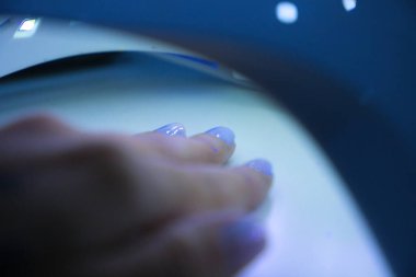 Bir kadının eli, güzellik salonundaki bir manikürcüde yeni cilalanmış tırnaklarını ultraviyole lambanın altında kurutuyor. Güzellik konsepti.