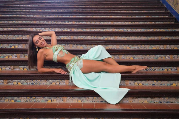 Genç ve güzel dansçı bir merdivende oturmuş dans mankeni pozları veriyor. Dansçı kırmızı bir elbise giyiyor. Göbek dansı konsepti.