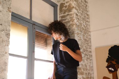 Stüdyonun penceresinde duran güzel kadın pencere camlarından çok mutlu görünüyor. Stüdyoda çok fazla doğal ışık var. İfadeleri ve ruh hallerini kavra.