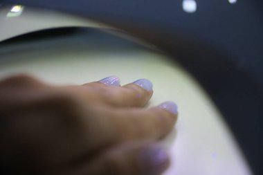 Bir kadının eli, güzellik salonundaki bir manikürcüde yeni cilalanmış tırnaklarını ultraviyole lambanın altında kurutuyor. Güzellik konsepti.