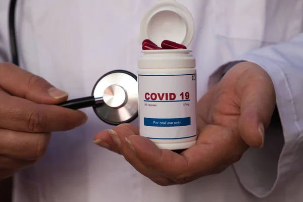 医生的手在医院里 一只手拿着一瓶白色的Covid 19抗病毒药 另一只手拿着听诊器 Covid 19抗逆转录病毒新药的概念 — 图库照片