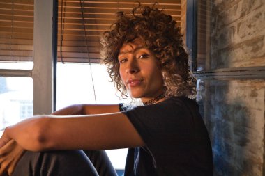 Stüdyoda büyük bir pencerenin kenarında oturan güzel bir kadın farklı neşe ve depresyon ifadeleri sergiliyor. Farklı ruh halleri kavramı.