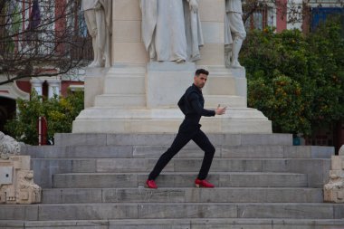 Siyah giyinmiş ve kırmızı ayakkabılar giyen genç ve yakışıklı bir adam Seville 'deki bir anıtın merdivenlerinde duruyor. İnsanlığın Flamenko kültürel mirası