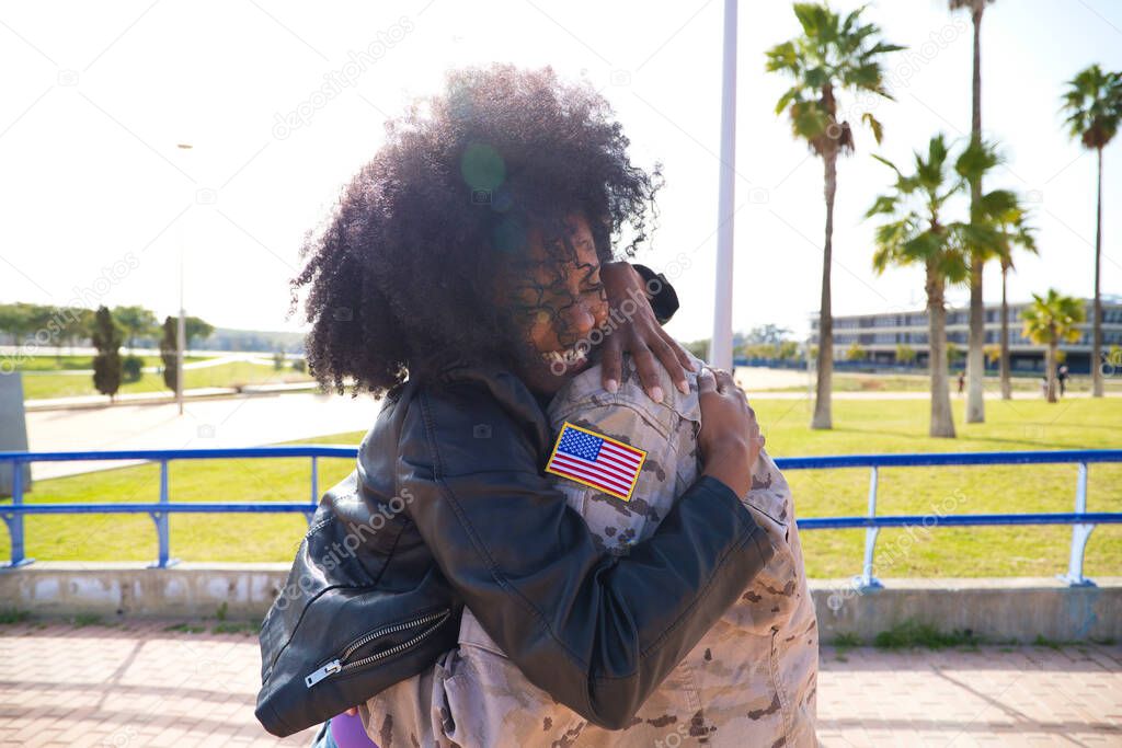 Afro-American woman and American soldier who has just arrived from the war on a peace mission embrace each other tightly. The woman is happy. Concept war and army, peace and mission.