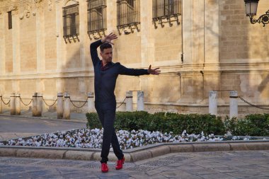 Genç ve yakışıklı adam flamenko yapıyor, siyah giyinmiş ve kırmızı ayakkabılar giyiyor, açık havada sokakta dans ediyor. İnsanlığın Flamenko kültürel mirası