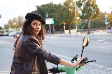 Koyu ve kıvırcık saçlı genç ve güzel bir kadın şehirde dolaşmak için elektrikli bir motosiklet sürerken Seville 'i geziyor. Yenilenebilir ve kirletici olmayan enerji. Turizm ve tatiller