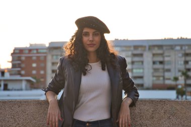 Kıvırcık kahverengi saçlı, siyah şapkalı, sıradan kıyafetler giymiş ve Sevilla 'yı gezen güzel bir genç kadının portresi. Arka planda güneş var. Turizm konsepti.