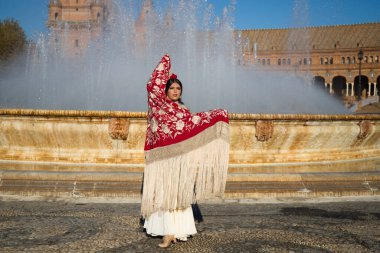 Flamenko dansçısı kadın, esmer ve güzel tipik İspanyol dansçı Seville meydanındaki bir çeşmenin önünde kırmızı bir manila şalıyla dans ediyor. İnsanlığın kültürel mirası Flamenko kavramı