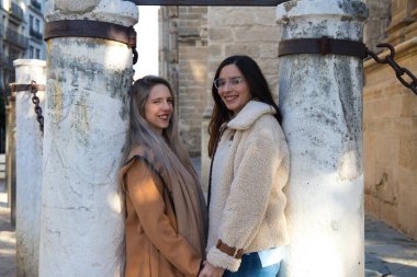 Gotik tarzı katedrali çevreleyen sütunlara yaslanan lezbiyen çift. Kadınlar birbirlerine aşkla ve mutlulukla bakıyorlar. Homoseksüel ve lezbiyen evlilik kavramı.