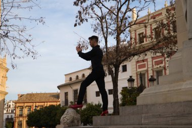 Siyah giyinmiş ve kırmızı ayakkabılar giyen genç ve yakışıklı bir adam Seville 'deki bir anıtın merdivenlerinde duruyor. İnsanlığın Flamenko kültürel mirası