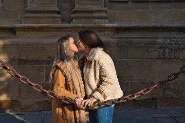 Gotik tarzı katedrali çevreleyen bir zincire yaslanan lezbiyen çift. Kadınlar tutkuyla ve aşkla öpüşüyorlar. Lezbiyen ve eşcinsel evlilik kavramı.