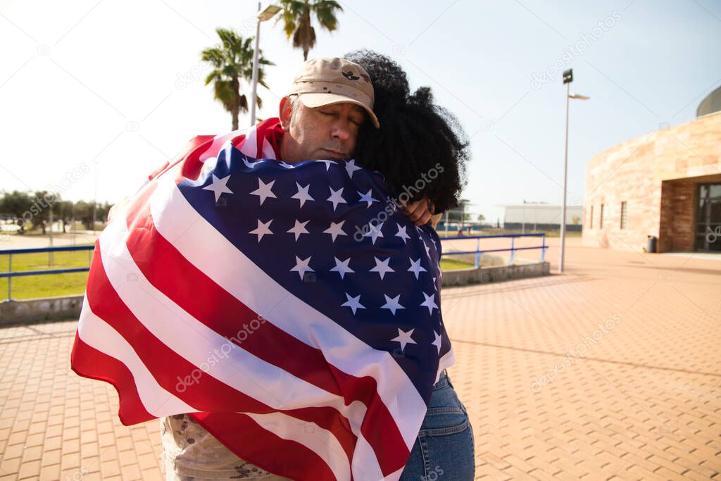 A beautiful afro-American woman and an American soldier embrace wrapped in the American flag. The soldier has returned from war and special missions. Concept of war and army.