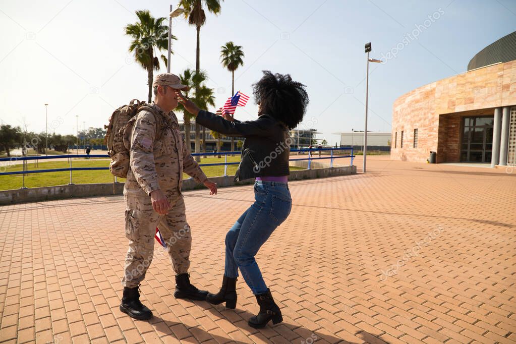 African-American woman with an American flag runs off in search of her soldier boyfriend who has come home from the war. They are going to melt in a loving embrace. Concept war, soldier, army, emotion