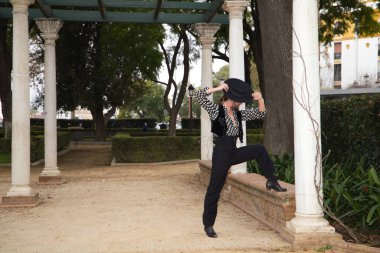 Çingene adam uzun saçlı ve sakallı flamenko dansı yapıyor mermer sütunların yanındaki parkta. Elinde siyah bir şapka tutuyor ve tutkuyla farklı duruşlar sergiliyor. Flamenko dansı.