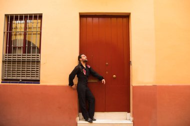 Kırmızı ahşap bir kapının arkasında siyah tişört ve kırmızı güllerle flamenko yapan bir adam, kapıya yaslanarak bekliyor. Flamenko dans konsepti insanlığın kültürel mirası.