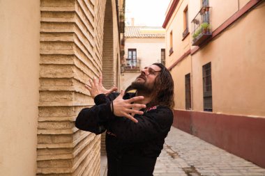 Siyah gömlek ve kırmızı güllerle flamenko dansı yapan uzun saçlı adam. Sevilla 'nın tipik dar bir sokağında elleriyle dans ediyor. Flamenko dans konsepti insanlığın kültürel mirası.