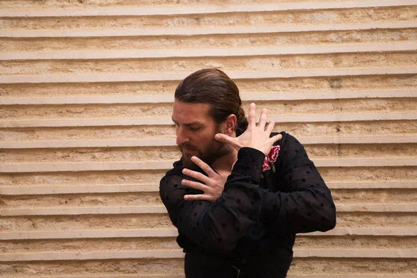 Siyah tişört ve kırmızı güllerle Flamenko yapan bir adamın portresi. Kahverengi arka planda elleriyle farklı pozlar veriyor. Tutkuyu. Flamenko dans konsepti insanlığın kültürel mirası.