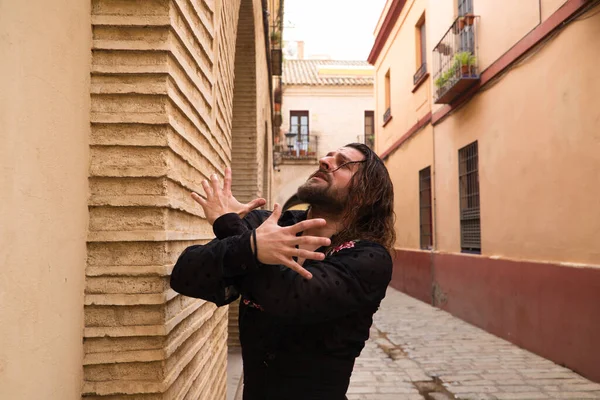 Siyah gömlek ve kırmızı güllerle flamenko dansı yapan uzun saçlı adam. Sevilla 'nın tipik dar bir sokağında elleriyle dans ediyor. Flamenko dans konsepti insanlığın kültürel mirası.