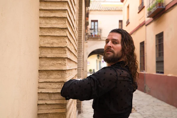 Siyah gömlek ve kırmızı güllerle flamenko dansı yapan uzun saçlı adam. Sevilla 'nın tipik dar bir sokağında elleriyle dans ediyor. Flamenko dans konsepti insanlığın kültürel mirası.