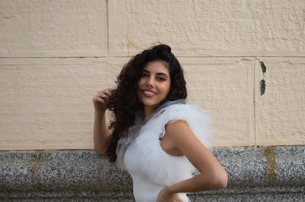 Genç, güzel, siyah, kıvırcık saçlı ve burnu kalkık bir kadın. Kadın, gri ve bej arkaplandaki fotoğraflara poz veriyor. Farklı ifadeler kullanıyor..