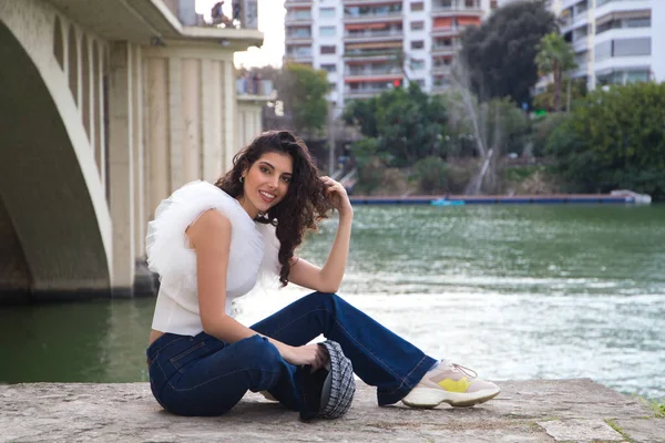 Genç, güzel, siyah, kıvırcık saçlı, şapkalı, nehir kenarında oturan bir kadın. Kadın fotoğraf için poz veriyor. Kavramsal ifadeler. Gülümse, üzül, düşün, eğlen, yaşa.