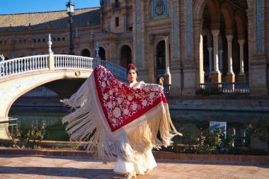 Flamenko dansçısı, kadın, esmer ve güzel tipik İspanyol dansçı Sevilla meydanında kırmızı bir manila şalıyla dans ediyor. İnsanlığın kültürel mirası Flamenko kavramı.